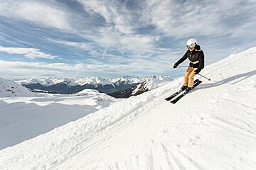 A person skiing down a snowy slope with mountains in the background