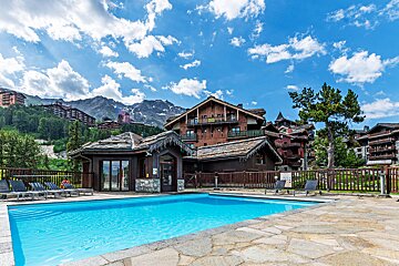 A large swimming pool in front of a building with mountains in the background