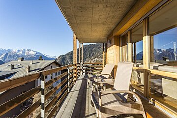 A balcony with chairs and a table with mountains in the background