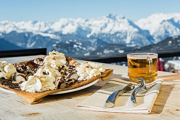 A plate of food and a glass of beer on a table with mountains in the background