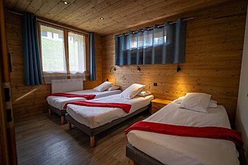 A bedroom with three beds and a window with blue curtains