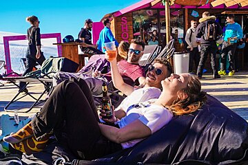 A woman laying on a bean bag chair holding a bottle of beer