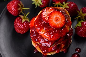 A stack of pancakes with strawberries and jam on top