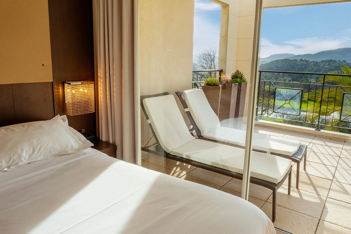 A hotel room with a bed and chairs on a balcony