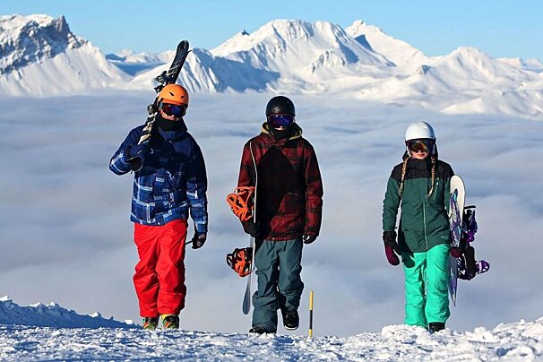 Three people standing on top of a snow covered mountain holding skis and snowboards