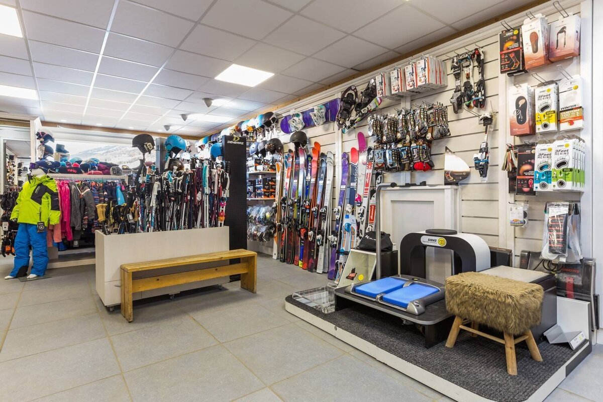 A brightly lit ski shop filled with skis, snowboards, helmets, winter apparel, and accessories. A foot fitting machine is visible on the right.