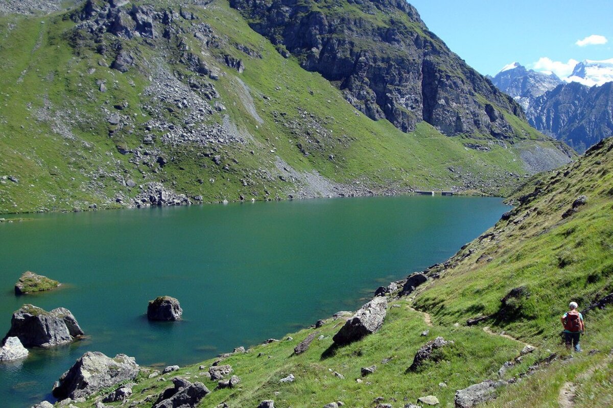 Two people are walking along a path near a lake in the mountains