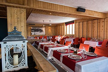A warm, wood-paneled restaurant interior with numerous tables set with red and white linens, ready for diners. A decorative white lantern sits prominently in the foreground.