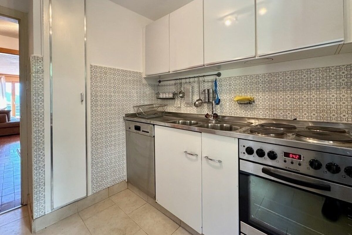 A compact kitchen featuring patterned backsplash tiles, white cabinets, a steel sink, and an oven.