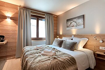 A cozy, wood-paneled bedroom features a large bed with a faux fur throw and white towels. Polar bear artwork hangs above the headboard, complemented by warm lighting.