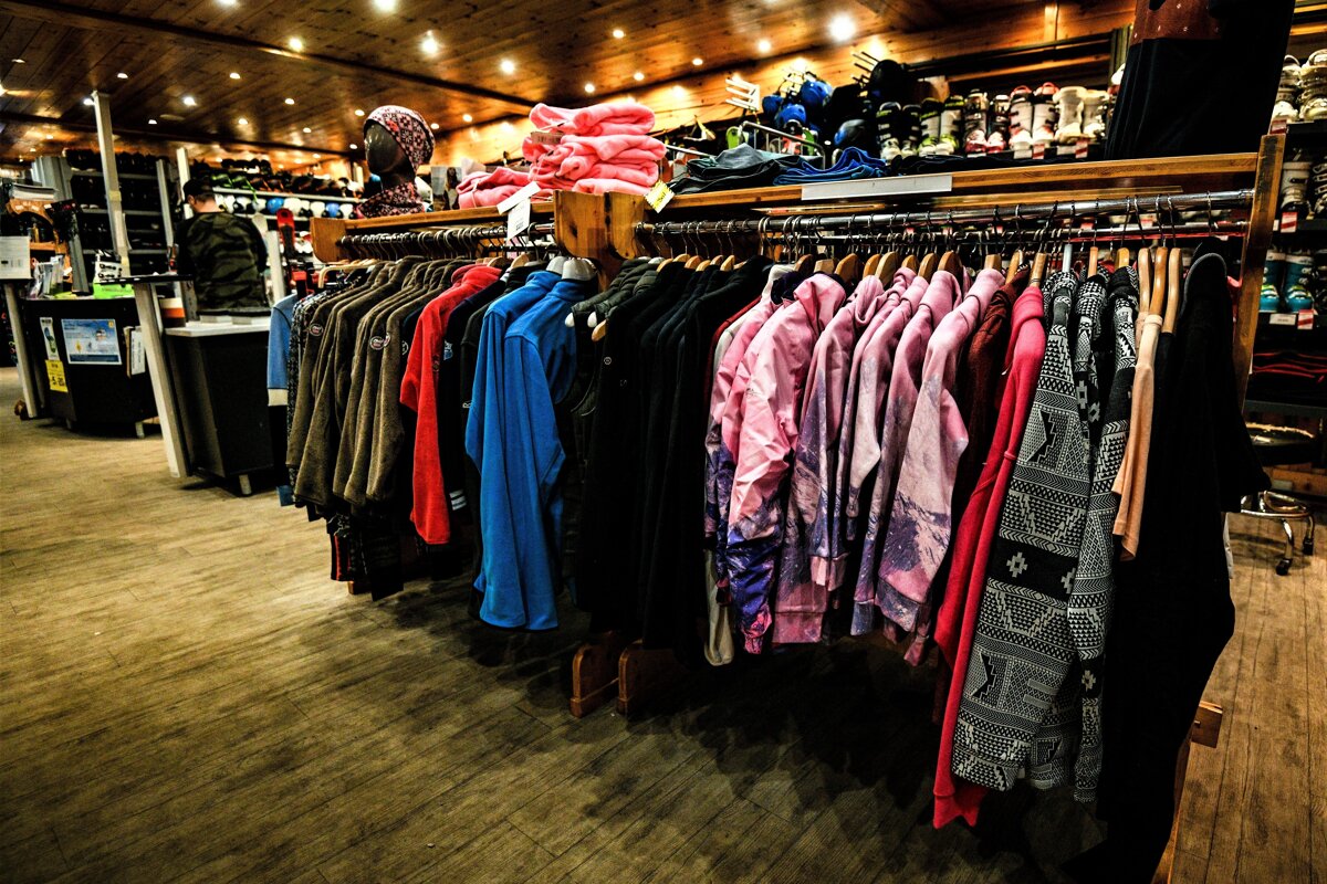 A cozy, brightly lit retail store showcasing racks of colorful winter and outdoor clothing, with ski boots and equipment visible in the background.