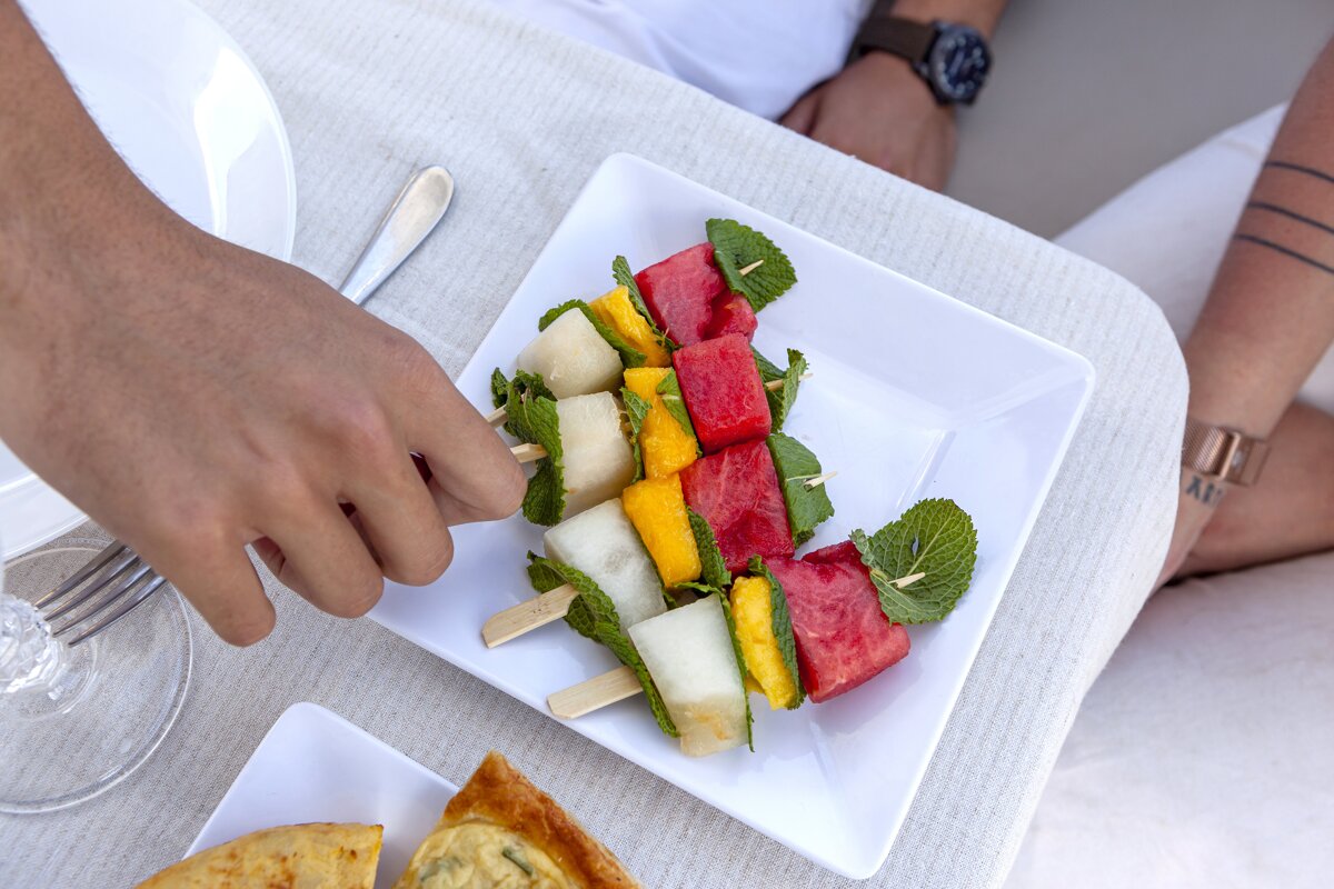 A person is eating a plate of fruit skewers