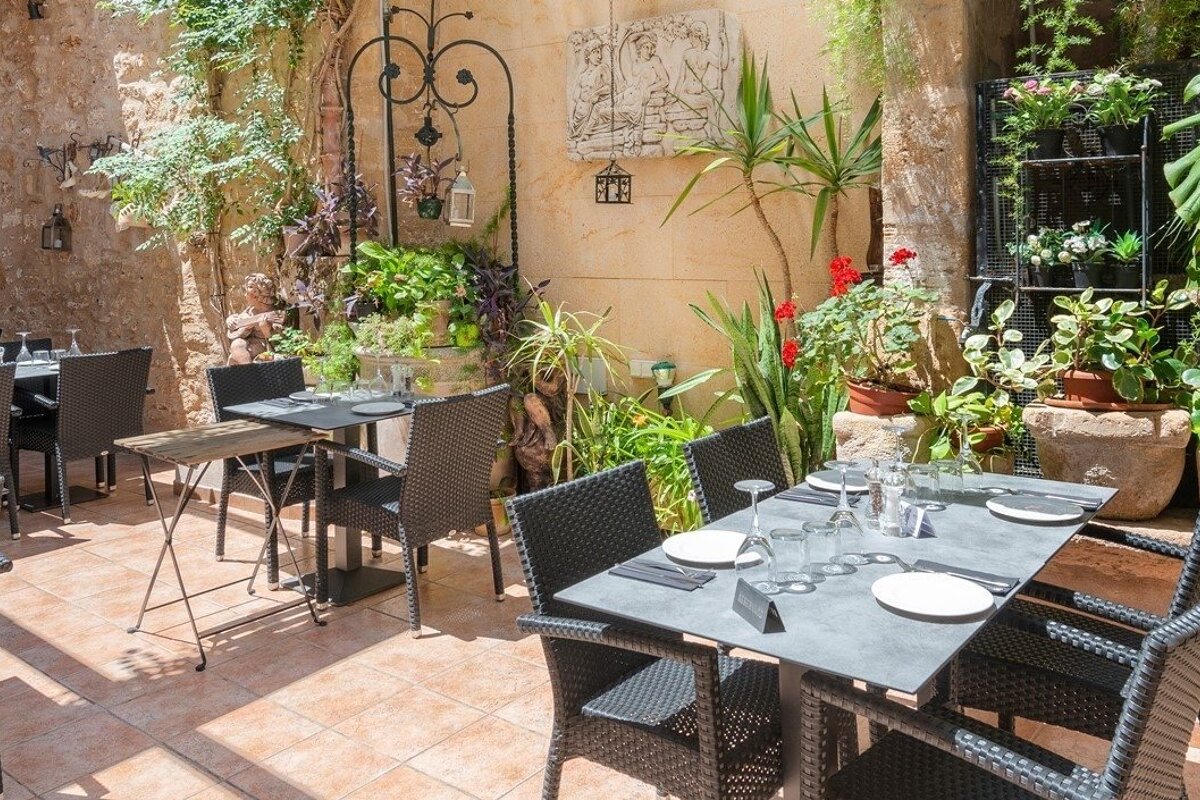 An inviting outdoor restaurant patio with set tables, black chairs, lush greenery, and rustic stone walls, perfect for dining al fresco.
