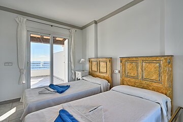 A bedroom with two beds and a balcony overlooking the ocean