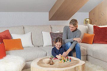 A woman and child sit on a couch playing with toys