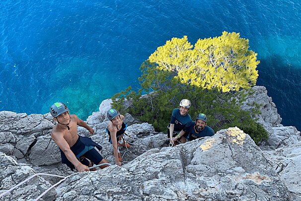 A group of people are climbing a rocky cliff near the ocean