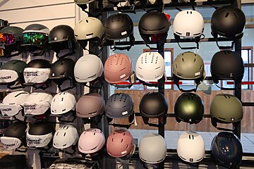 A vibrant retail display features numerous ski and snowboard helmets in various colors, including brands like Salomon and Smith, for winter sports.