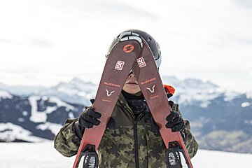 A person holding a pair of blizzard skis in front of their face