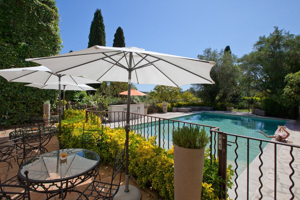 A swimming pool with a table and chairs under umbrellas