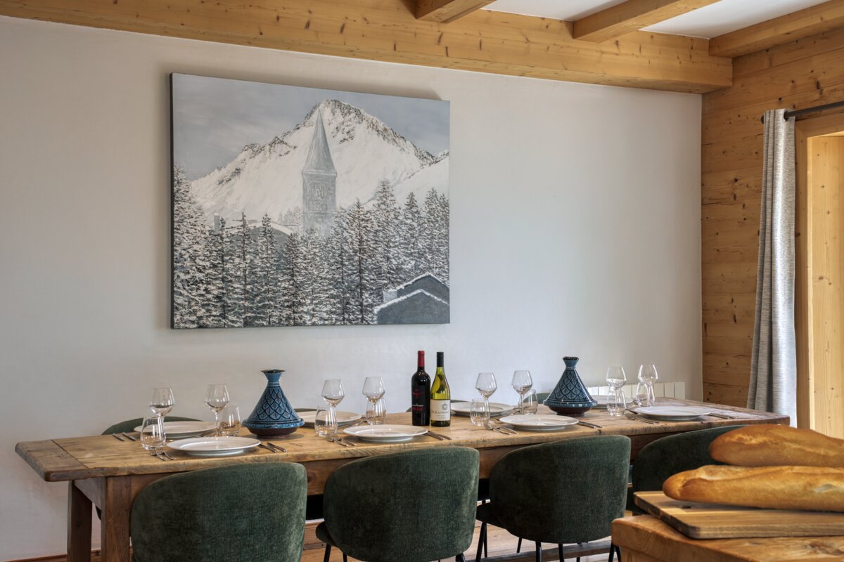 A dining room table with a painting of a mountain on the wall above it