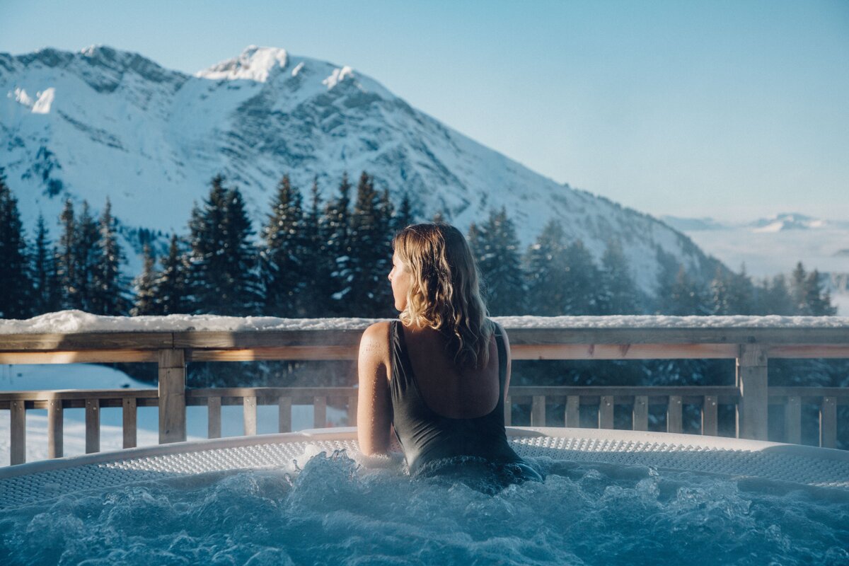 A woman sits in a hot tub with mountains in the background