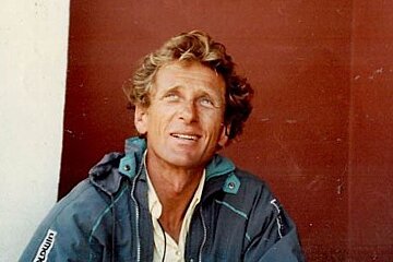 A man in a blue jacket is sitting in front of a red wall