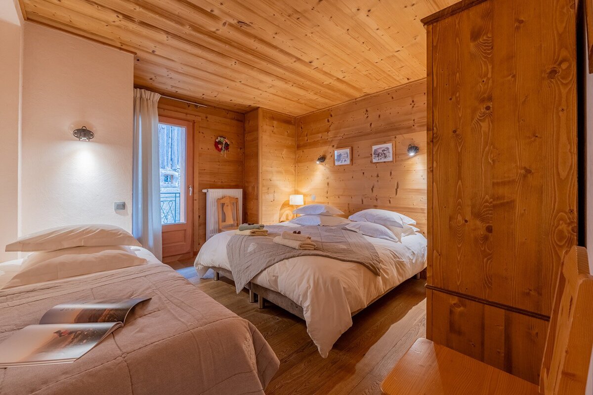 Warm, wood-paneled bedroom with two beds (one double, one single) and a balcony door. Cozy, rustic chalet style.