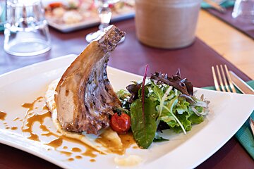 A gourmet lamb chop on mashed potatoes with gravy, fresh salad, and a cherry tomato, elegantly plated in a restaurant setting.