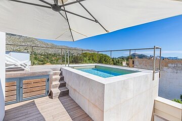 Sunny rooftop terrace with a small plunge pool, wooden deck, and a large umbrella, offering panoramic mountain views under a clear blue sky.