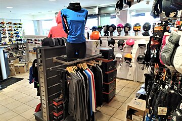 An indoor sports gear shop, likely for skiing or snowboarding, displaying helmets, goggles, and clothing on mannequins and racks.
