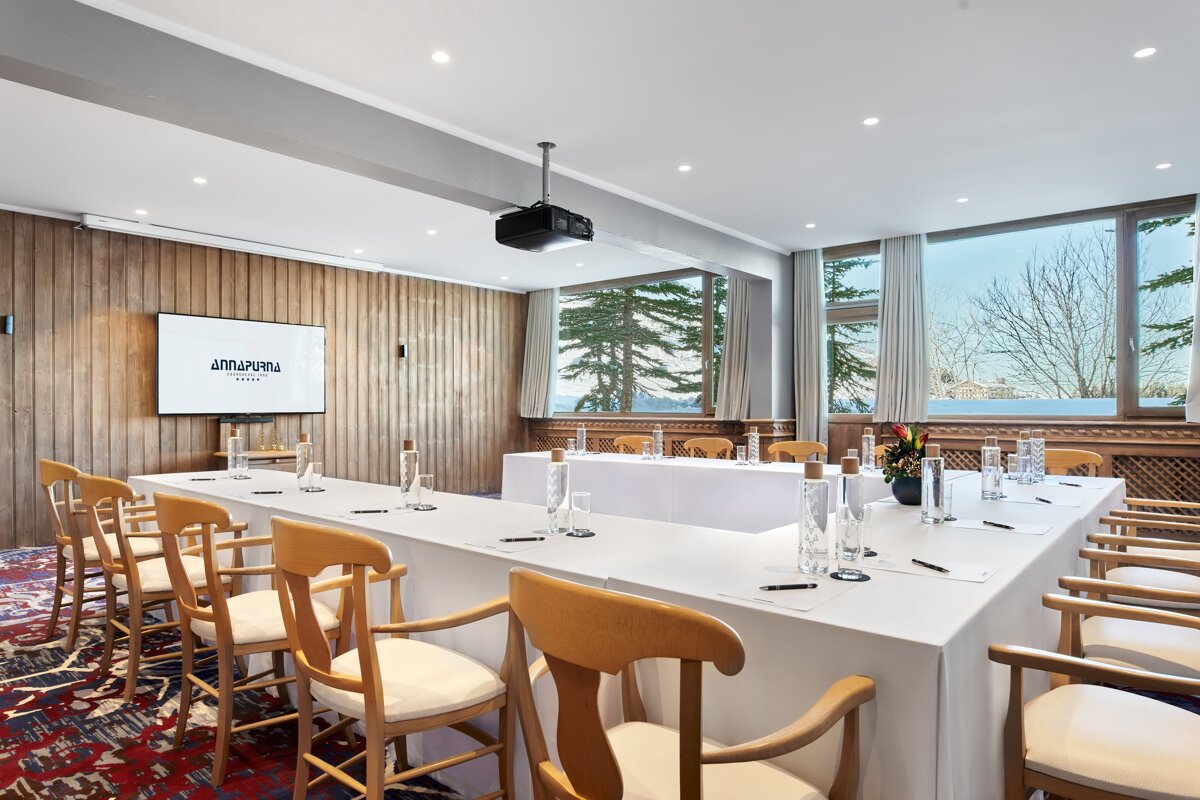 A conference room with long tables and chairs and a projector screen that says amurpura