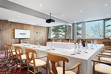 A conference room with long tables and chairs and a projector screen that says amurpura