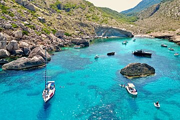 A few boats are in the water near a rocky shoreline