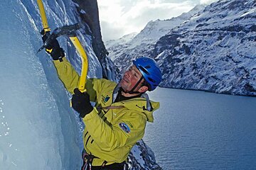 a man ice climbing above a lake on a frozen waterfall