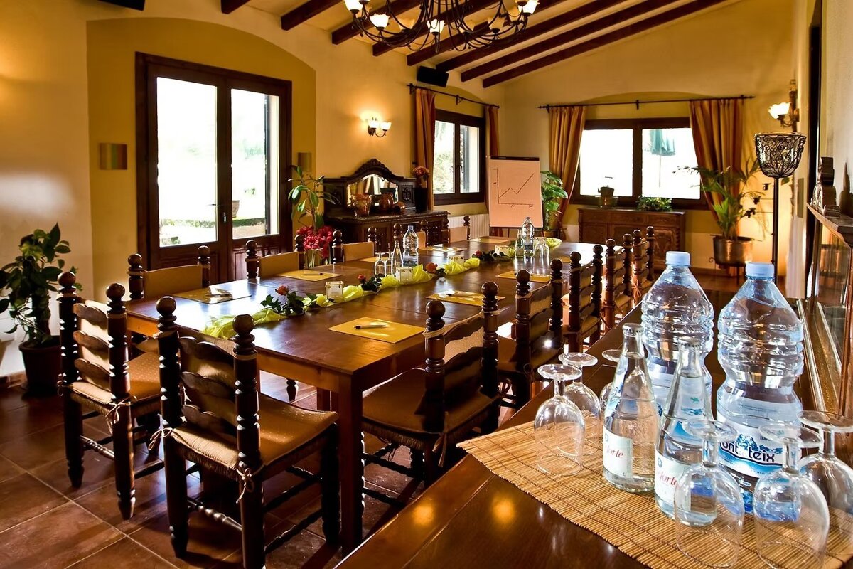 A rustic, warmly lit conference room with a long wooden table set with water bottles and glasses, and a flipchart in the corner.