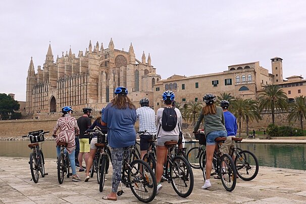 cyclists on a tour past the cathedral in palma de mallorca