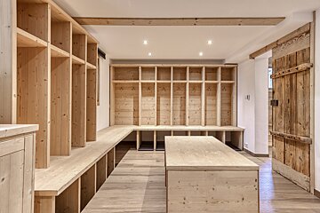 A bright room with extensive natural wood shelving, built-in benches, a central table, and a rustic plank door, creating a warm, organized space.