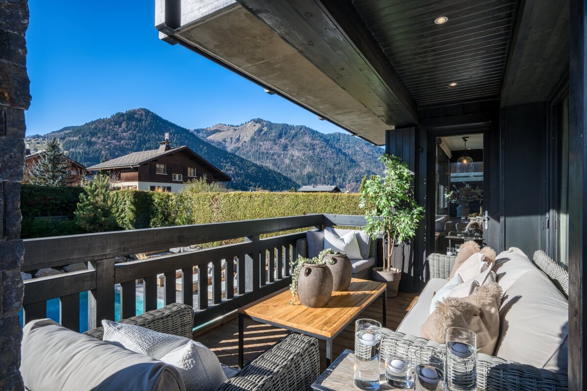A balcony with a couch and a table with mountains in the background