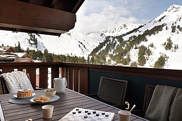 A wooden balcony set with snacks and checkers, offering a scenic view of snow-covered alpine mountains.
