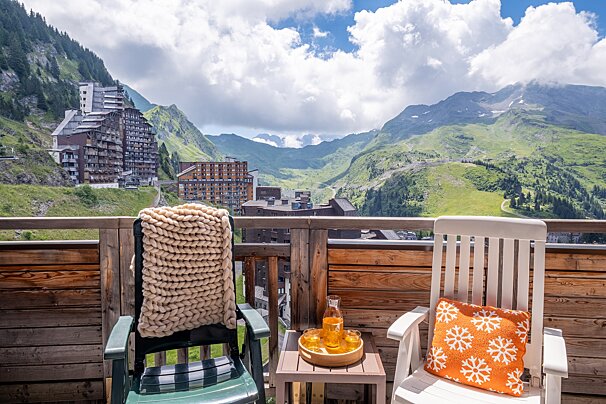 A chair with a snowflake pillow sits on a balcony overlooking mountains