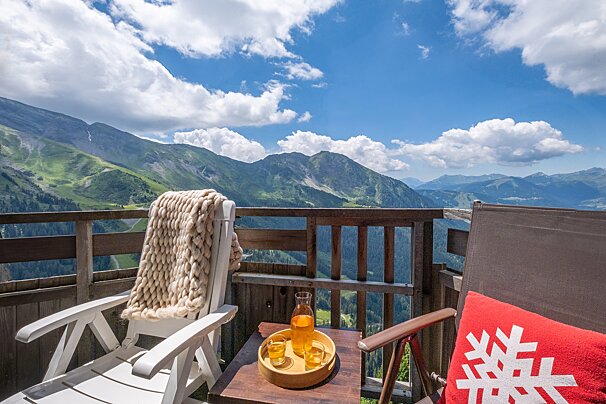 A chair with a snowflake pillow sits on a balcony overlooking the mountains