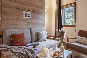 Cozy living room featuring a grey sofa, a wooden Murphy bed wall, and a coffee table with tea, pastries, and a window view.