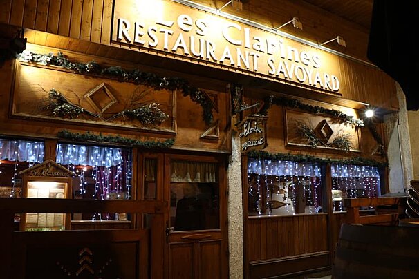 A restaurant called les clarines savoyard is lit up at night
