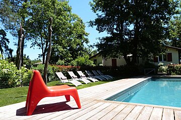 A red chair sits on a wooden deck next to a swimming pool
