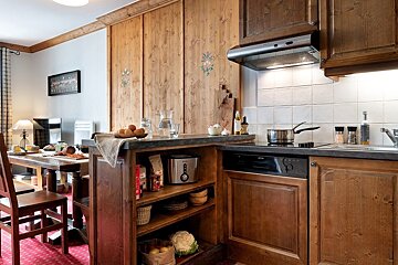Cozy rustic kitchen with wooden cabinets, a stove, counter space, and a dining table set in the background.