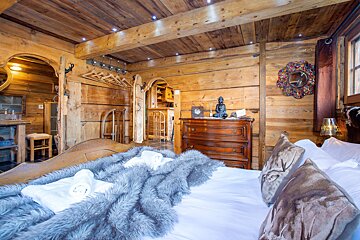 A cozy, rustic wooden bedroom with a bed, grey faux-fur throw, Buddha statue on a dresser, and unique chalet decor.