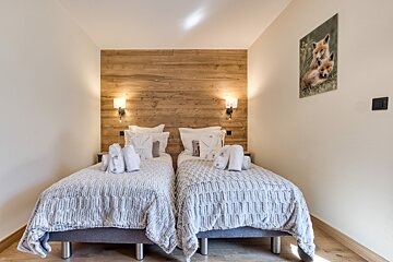 A warm bedroom with two twin beds, white & grey bedding, and a rustic wood headboard with sconces. A picture of two foxes hangs on the light wall.
