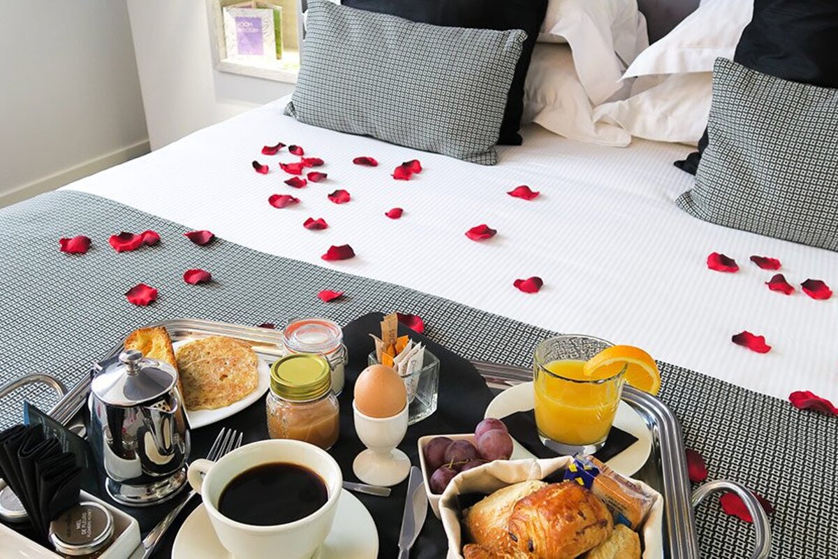 A tray of food on a bed with rose petals on it