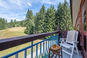 A rocking chair sits on a balcony overlooking a forest