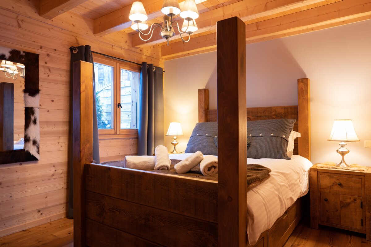 A cozy, wood-paneled chalet bedroom with a large wooden four-poster bed, warm lighting, and rustic decor.